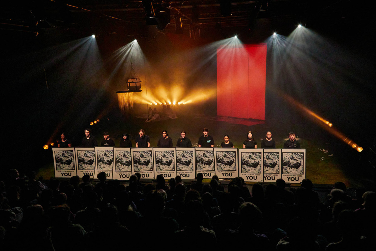 12 junge Menschen die in einer Reihe stehen und Plakate mit der Aufschrift &raquo;Your Country needs You&laquo; hochhalten