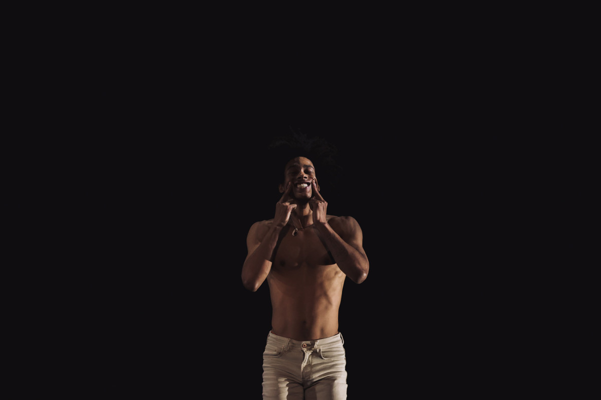 Ein Schwarzer T&auml;nzer, der seinen Mund mit den H&auml;nden zu einem L&auml;cheln verzieht