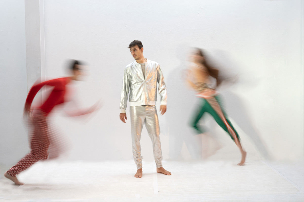 Eine bewegunsunscharfe Aufnahme von drei T&auml;nzer*innen in einem wei&szlig;en Raum