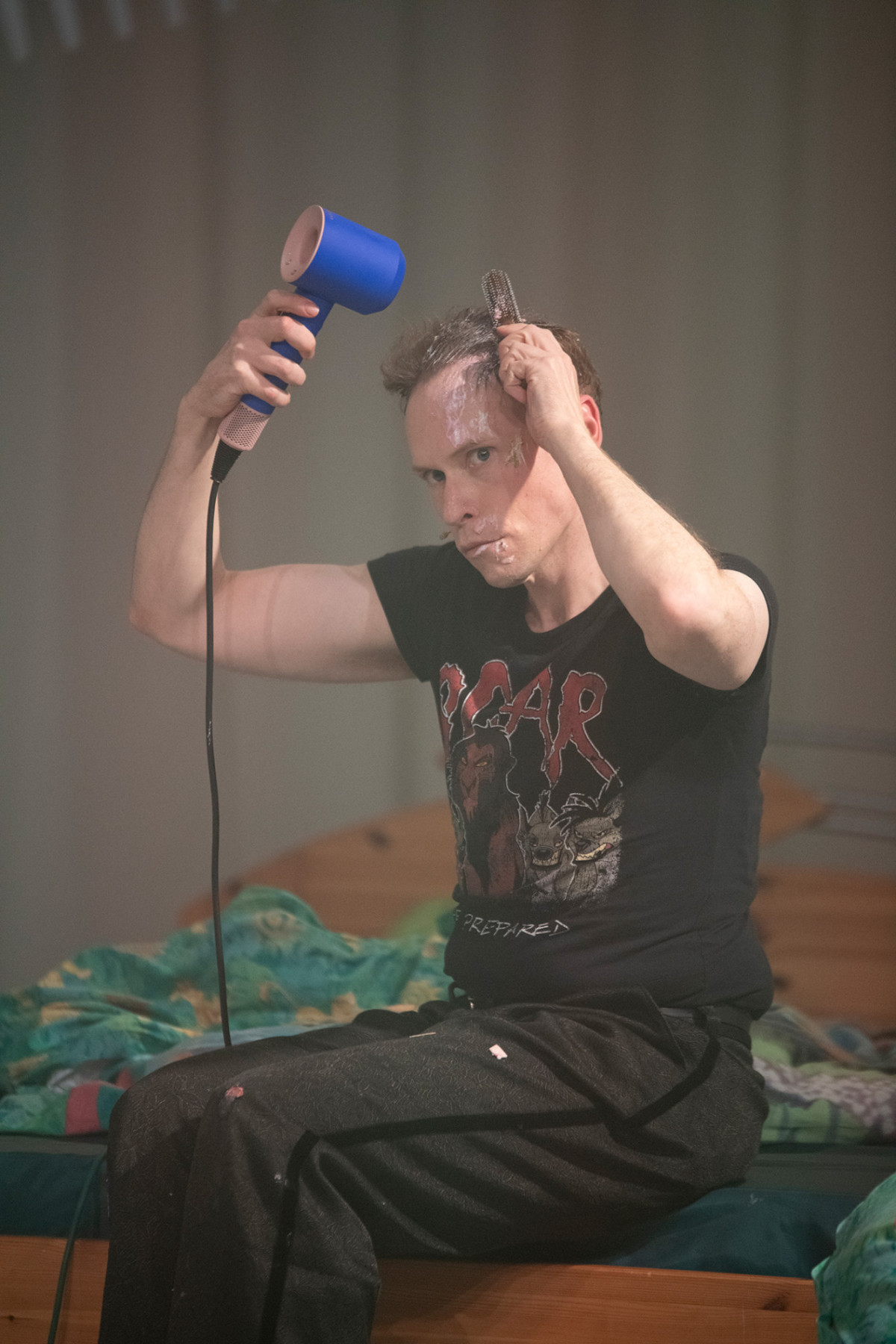 Henrik Quast sitzt auf einem Bett und f&ouml;hnt sein weniges Haar