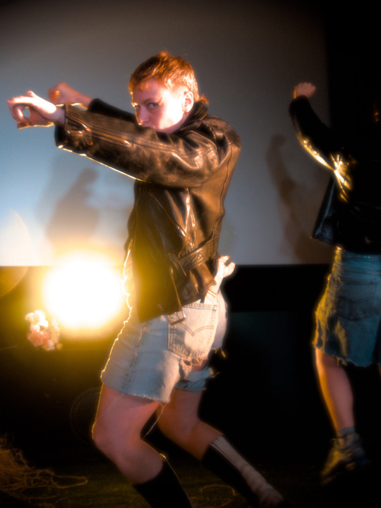 Eine Butch in Lederjacke macht eine Motorrad-Pantomime