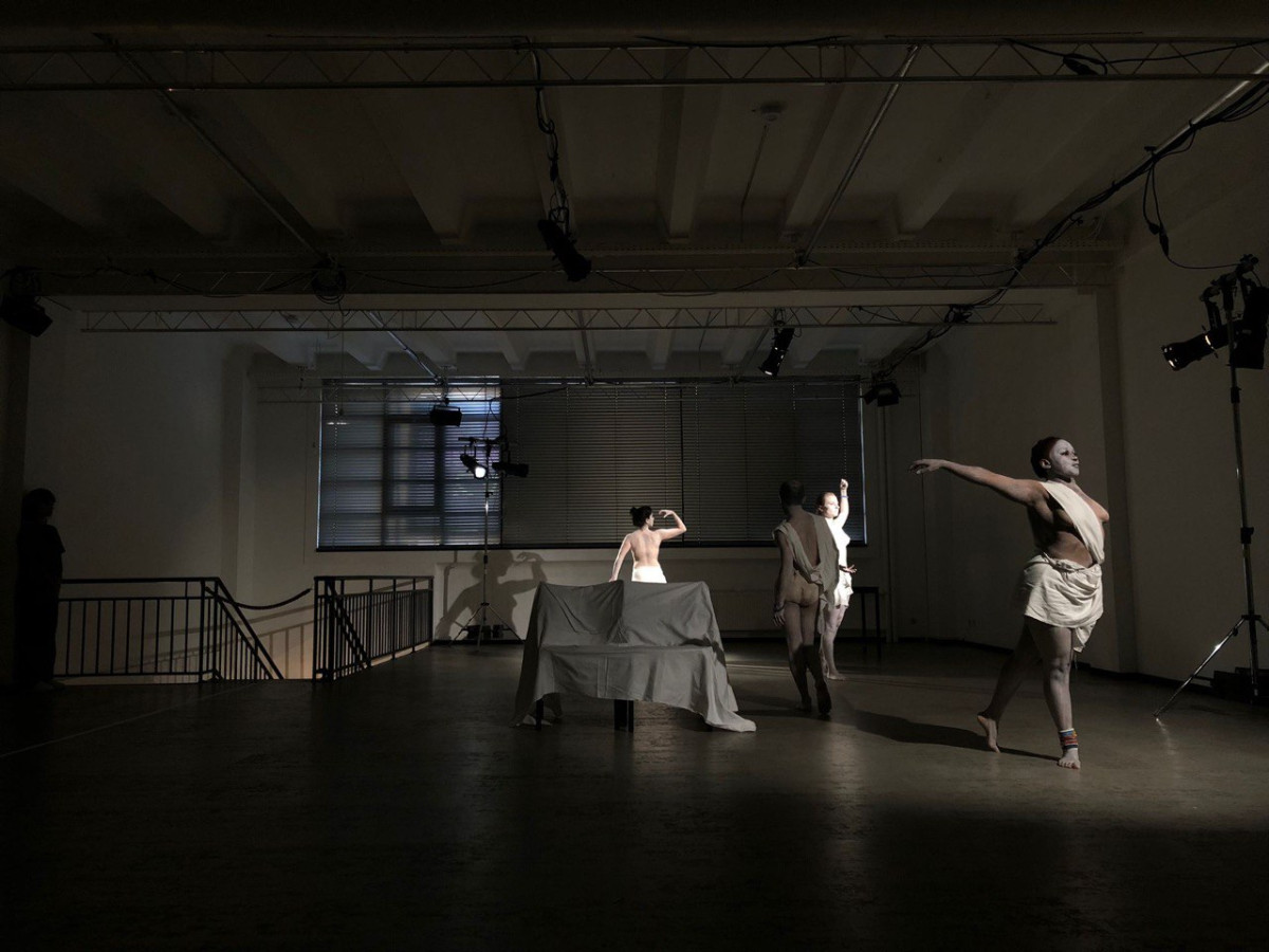 Three people with their skin painted white pose like statues in a dimly lit room