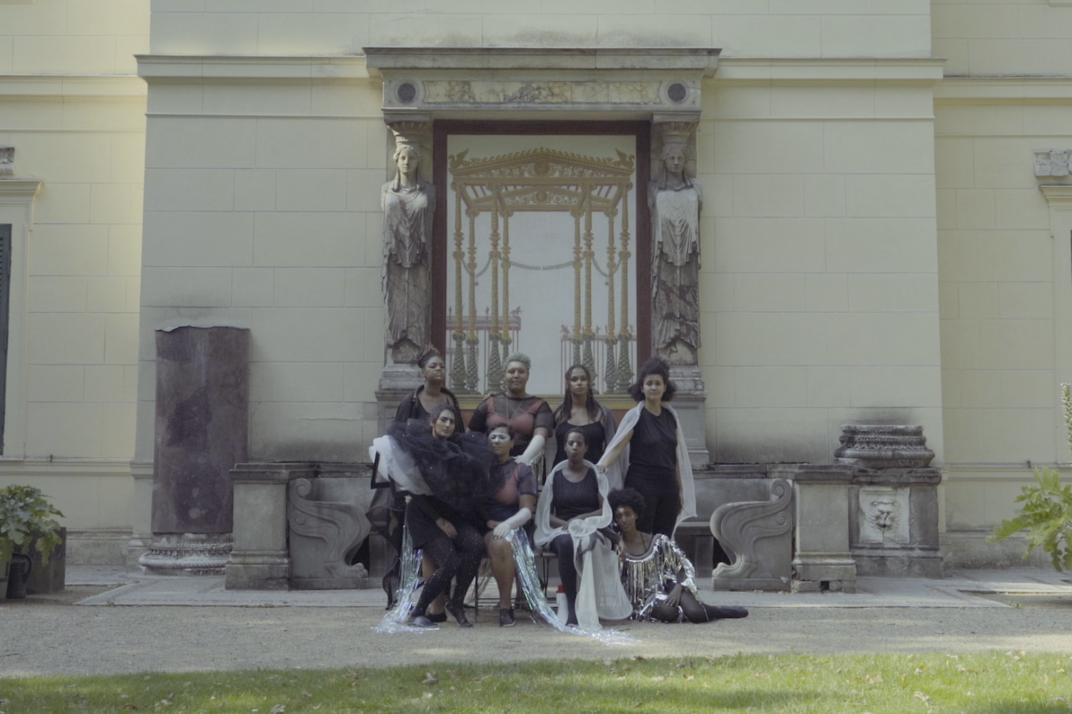 Performer*innen in prachtvollen Kostümen posieren vor einem Schloss