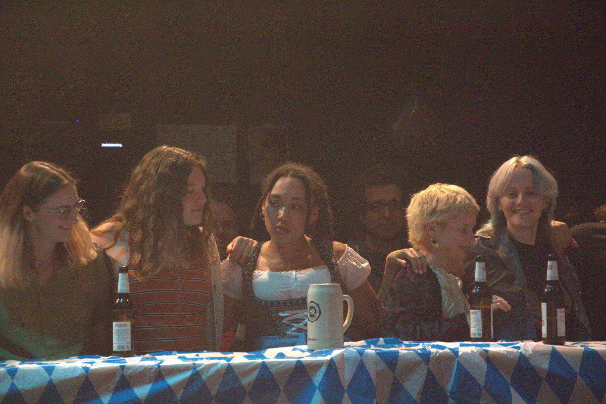 Tamira Kalmbach in a dirndl, sitting on a beer bench surrounded by laughing people