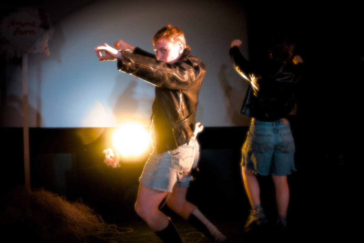 A person wearing denim shorts and a leather jacket striking a rodeo pose