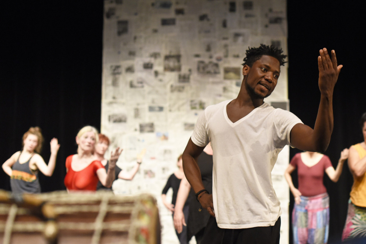 Person im Vordergrund posiert mit erhobenener Hand, Personen im Hintergrund in gleicher Pose.