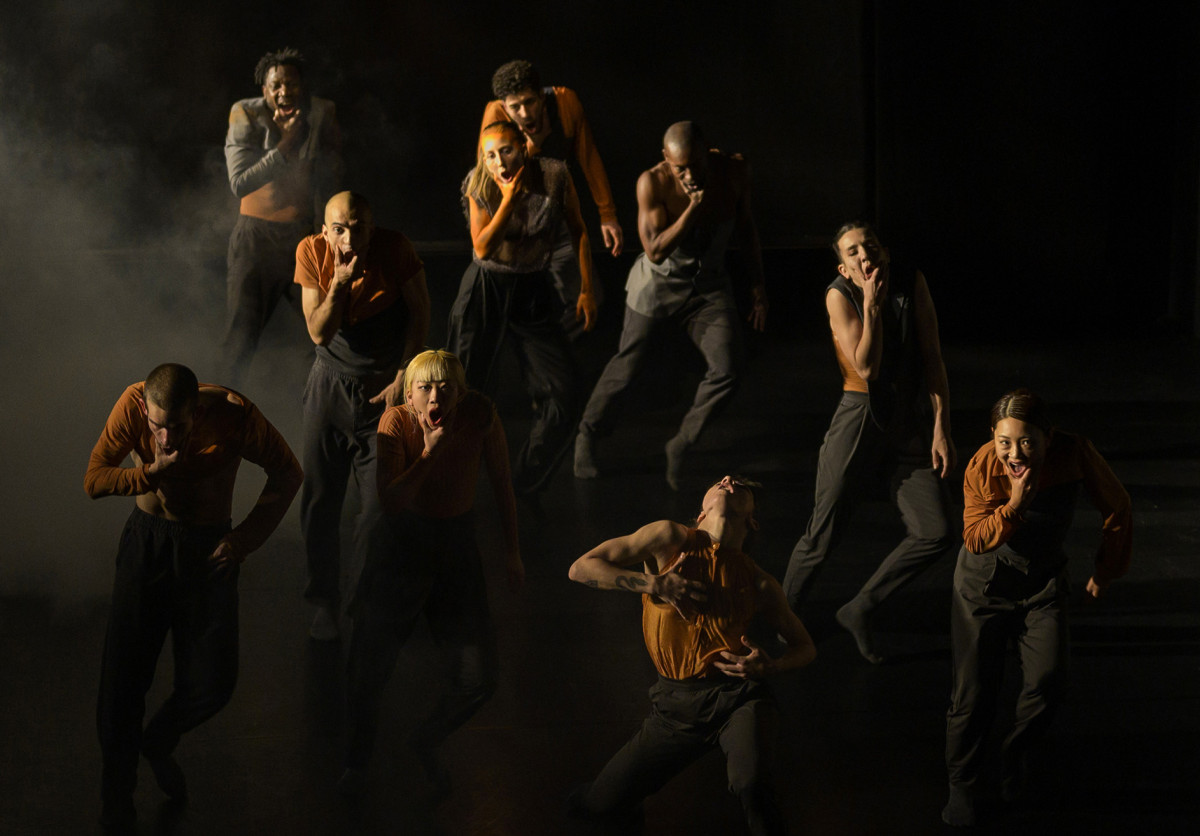 10 Performerinnen fassen sich ins Gesicht und haben verzerrte Mimik. Auf der B&uuml;hne ist es dunkel und neblig.